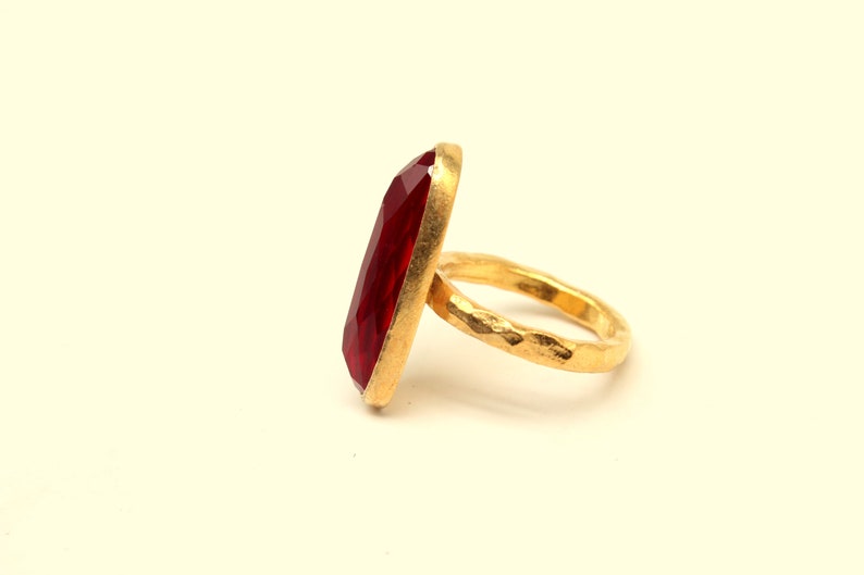 May include: A gold ring with a large, red, faceted gemstone. The band of the ring is textured.