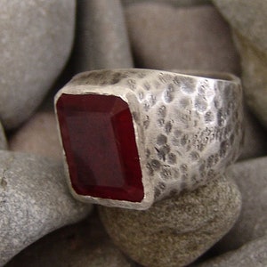 May include: A silver ring with a hammered finish and a large, rectangular, dark red gemstone.