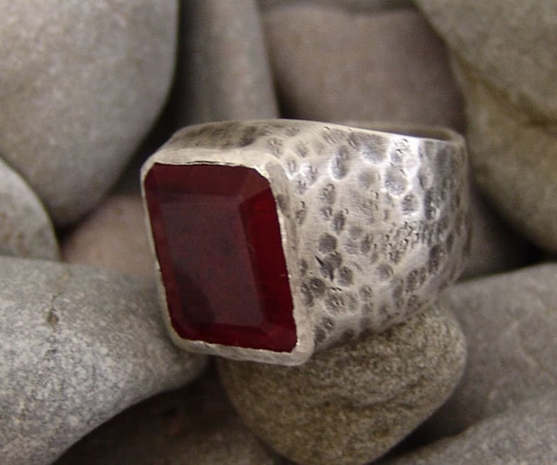 May include: A silver ring with a hammered finish and a large, rectangular, dark red gemstone.