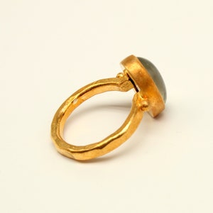 May include: A gold ring with a gray gemstone set in a bezel setting. The ring band is textured and has a hammered finish.
