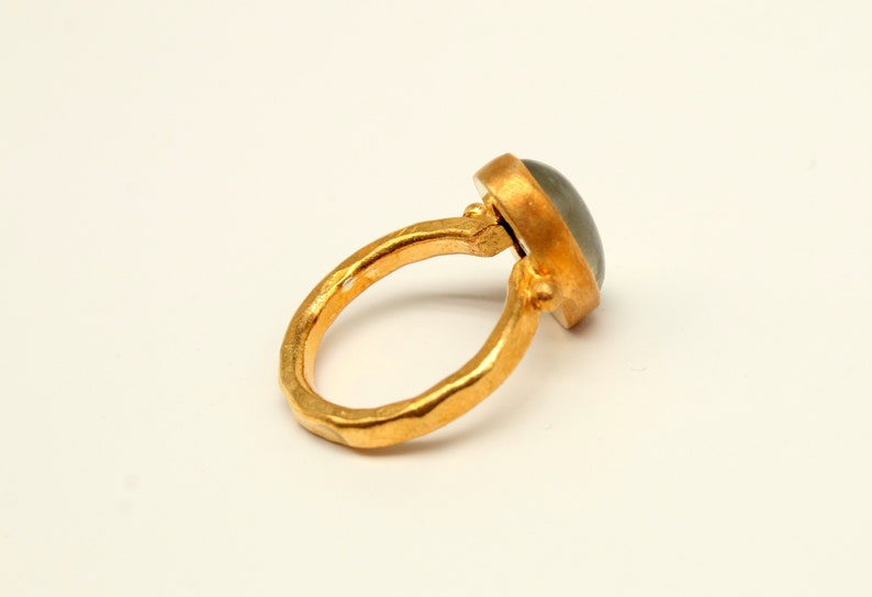 May include: A gold ring with a gray gemstone set in a bezel setting. The ring band is textured and has a hammered finish.