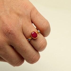 Peut inclure: Une bague en or avec une grande pierre de rubis ovale et de plus petites pierres bleues sur la bande.