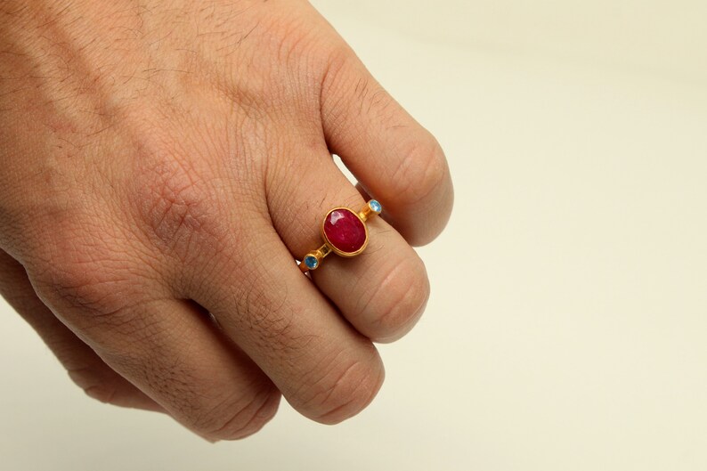Peut inclure: Une bague en or avec une grande pierre de rubis ovale et de plus petites pierres bleues sur la bande.