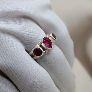 Pu&ograve; includere: Un anello d'argento con tre pietre ovali rosa incastonate in una fascia.