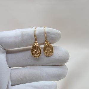 May include: A pair of gold dangle earrings with a detailed design. The earrings are oval shaped and have a hook closure.