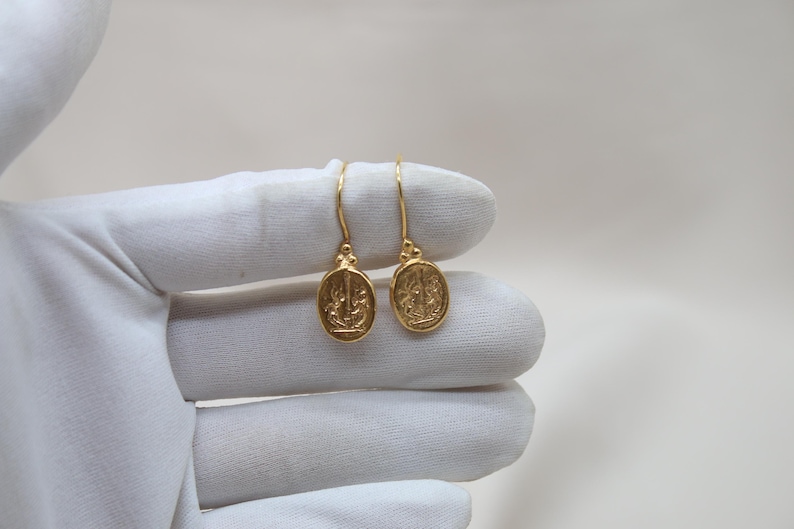 May include: A pair of gold dangle earrings with a detailed design. The earrings are oval shaped and have a hook closure.