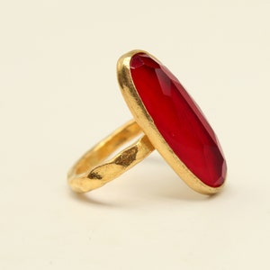 May include: A gold ring with a large, oval-shaped, red gemstone.