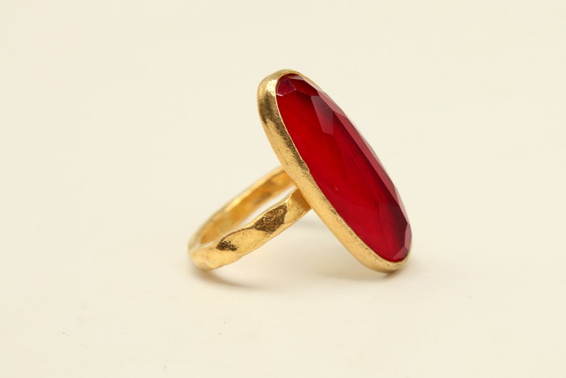 May include: A gold ring with a large, oval-shaped, red gemstone.