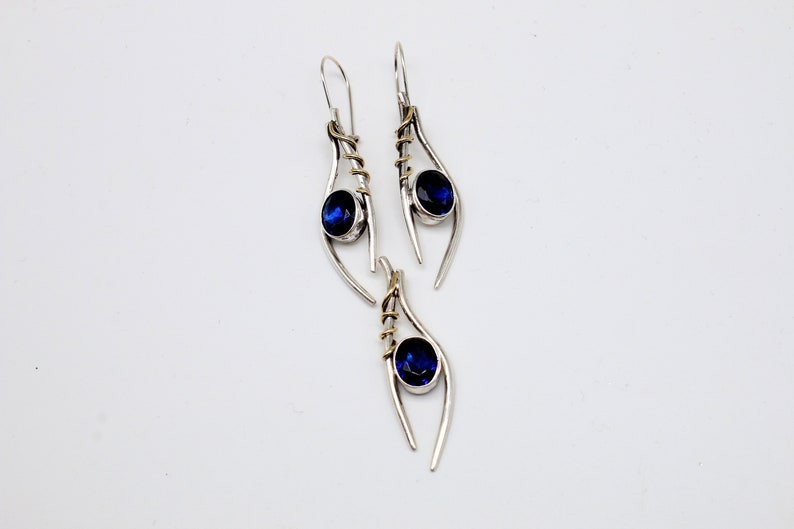 May include: A pair of silver earrings with blue gemstones and gold accents. The earrings are shaped like a teardrop with a curved line.