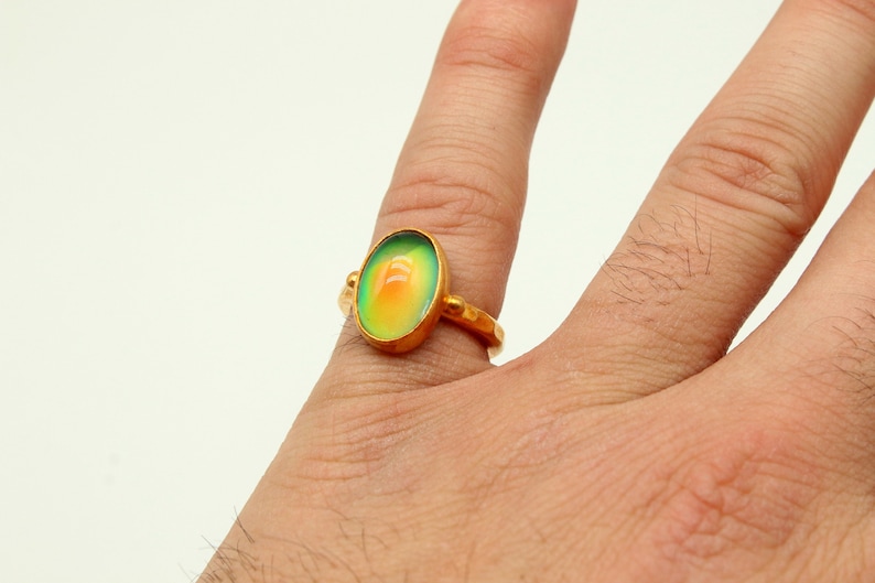 May include: A gold ring with a large oval-shaped iridescent gemstone. The gemstone is green, yellow, and orange.