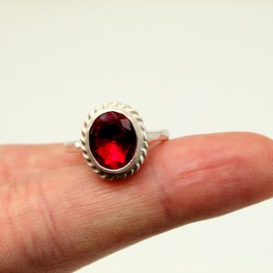 Op de afbeelding: Een zilveren ring met een rode, ovale edelsteen gezet in een touwachtige rand.