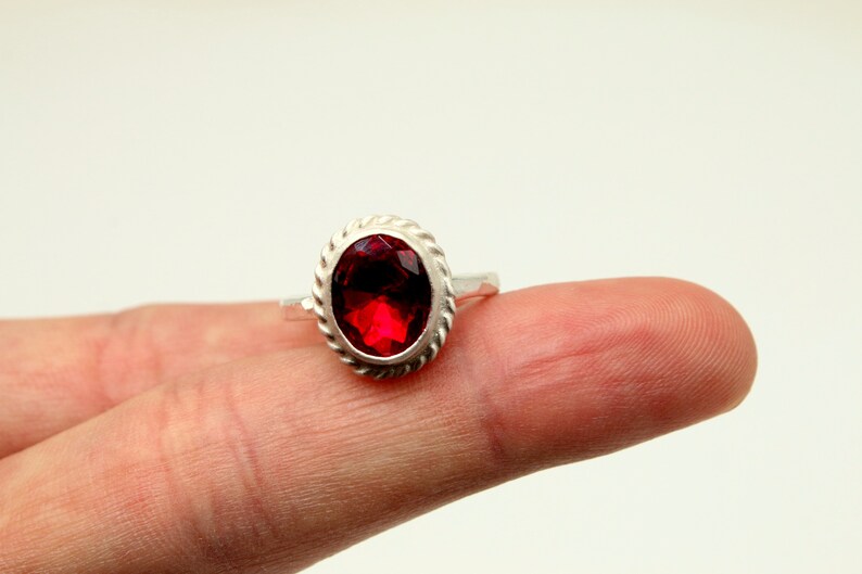 Op de afbeelding: Een zilveren ring met een rode, ovale edelsteen gezet in een touwachtige rand.