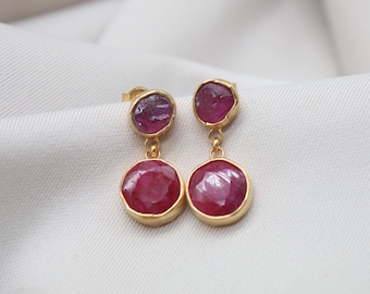 May include: Gold earrings with two round pink gemstones. The earrings have a dangling design.