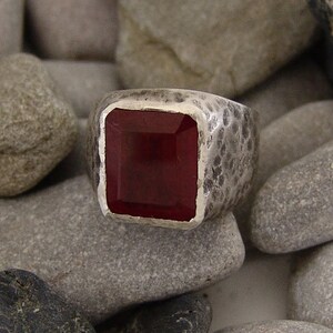 May include: A silver ring with a textured band and a square, dark red gemstone.