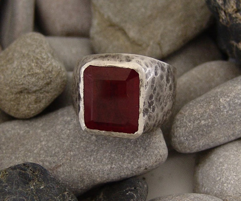 May include: A silver ring with a textured band and a square, dark red gemstone.