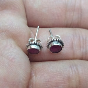 May include: A pair of silver stud earrings with a small, round, dark red gemstone in each earring.