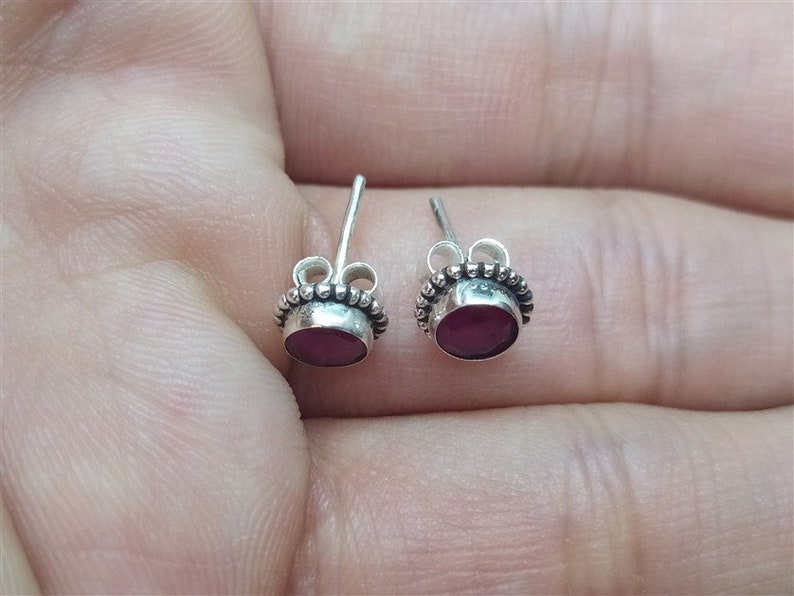 May include: A pair of silver stud earrings with a small, round, dark red gemstone in each earring.