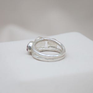 Pu&ograve; includere: Un anello d'argento con una pietra preziosa rossa incastonata nella fascia. L'anello &egrave; composto da due fasce intrecciate.