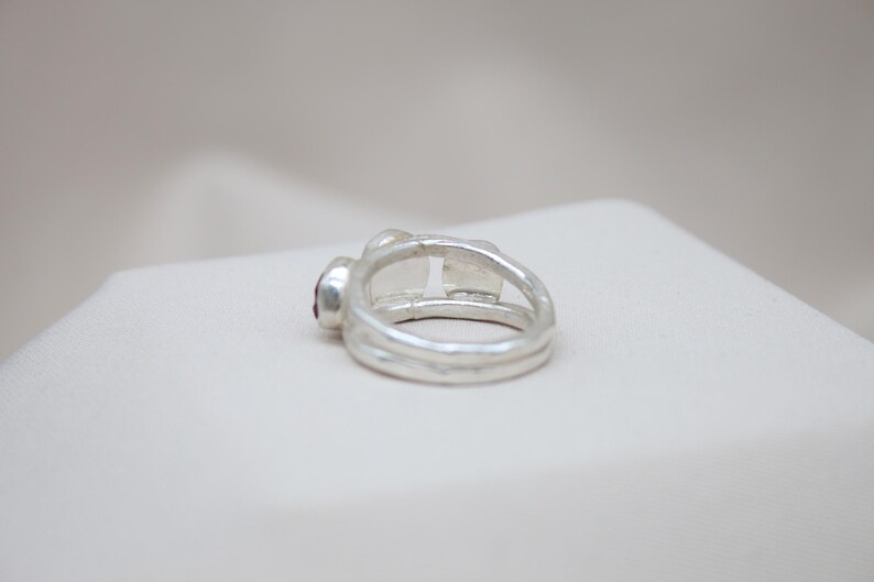 Pu&ograve; includere: Un anello d'argento con una pietra preziosa rossa incastonata nella fascia. L'anello &egrave; composto da due fasce intrecciate.