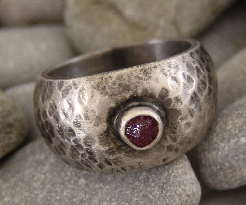 May include: A silver ring with a hammered texture and a single red gemstone set in the centre.
