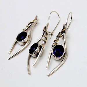 May include: A pair of silver earrings with blue gemstones and gold accents. The earrings are designed with a curved, organic shape.