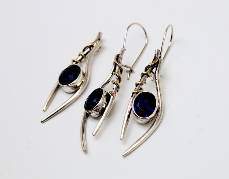 May include: A pair of silver earrings with blue gemstones and gold accents. The earrings are designed with a curved, organic shape.