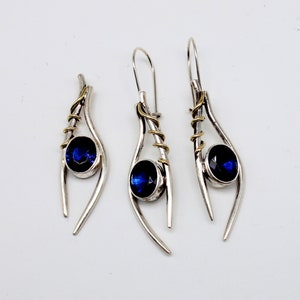 May include: A set of three silver earrings with blue gemstones and gold accents. The earrings are designed in a teardrop shape with a twisted wire detail.