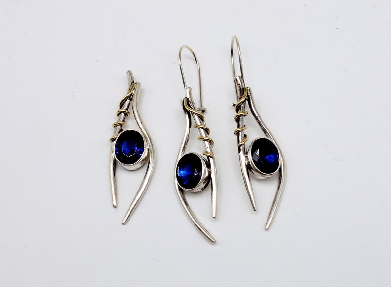 May include: A set of three silver earrings with blue gemstones and gold accents. The earrings are designed in a teardrop shape with a twisted wire detail.