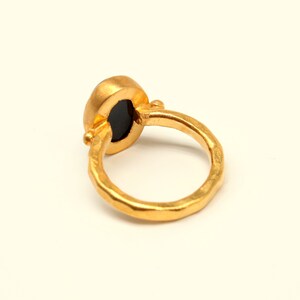 May include: A gold ring with a black oval gemstone. The ring has a hammered texture.