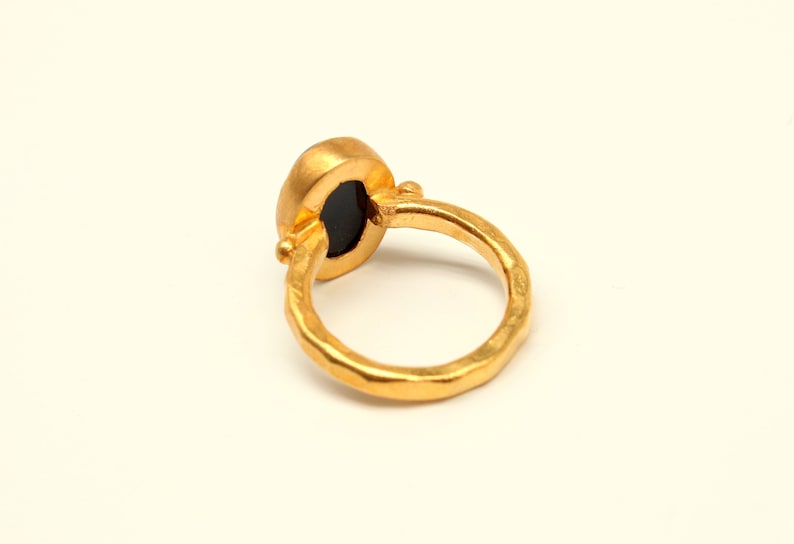May include: A gold ring with a black oval gemstone. The ring has a hammered texture.