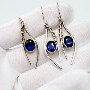 May include: A pair of silver earrings with blue gemstones and gold accents. The earrings are shaped like teardrops and have a delicate, whimsical design.