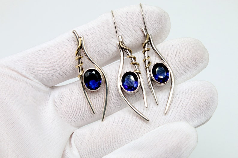 May include: A pair of silver earrings with blue gemstones and gold accents. The earrings are shaped like teardrops and have a delicate, whimsical design.