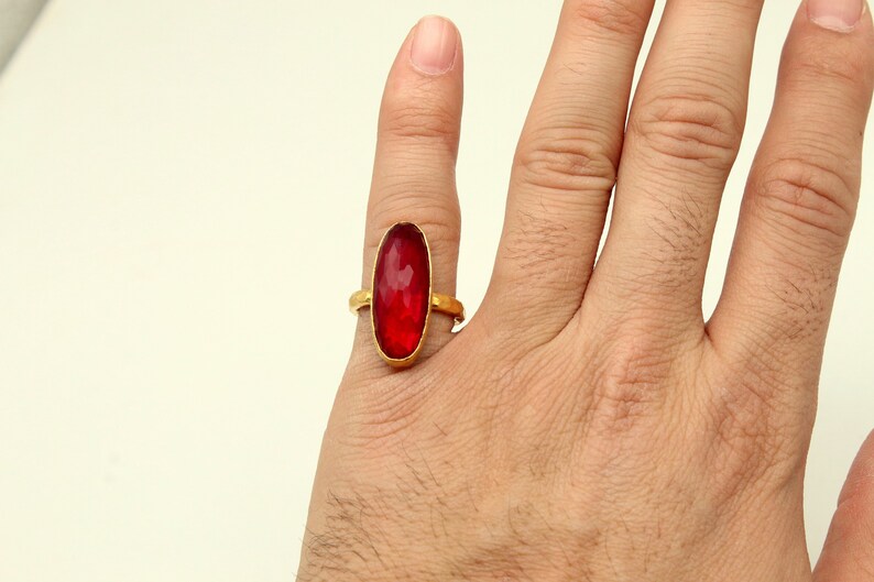 Może przedstawiać: Złoty pierścionek z dużym, owalnym, czerwonym kamieniem szlachetnym.