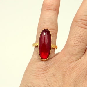 Może przedstawiać: Złoty pierścionek z dużym, owalnym, czerwonym kamieniem szlachetnym.