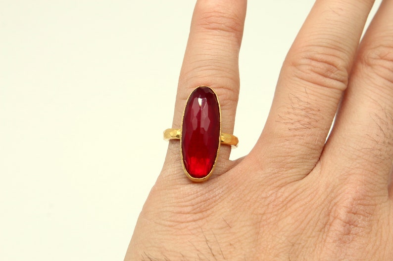 Może przedstawiać: Złoty pierścionek z dużym, owalnym, czerwonym kamieniem szlachetnym.