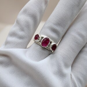 Pu&ograve; includere: Un anello d'argento con tre pietre preziose rosa di forma ovale incastonate nella fascia.