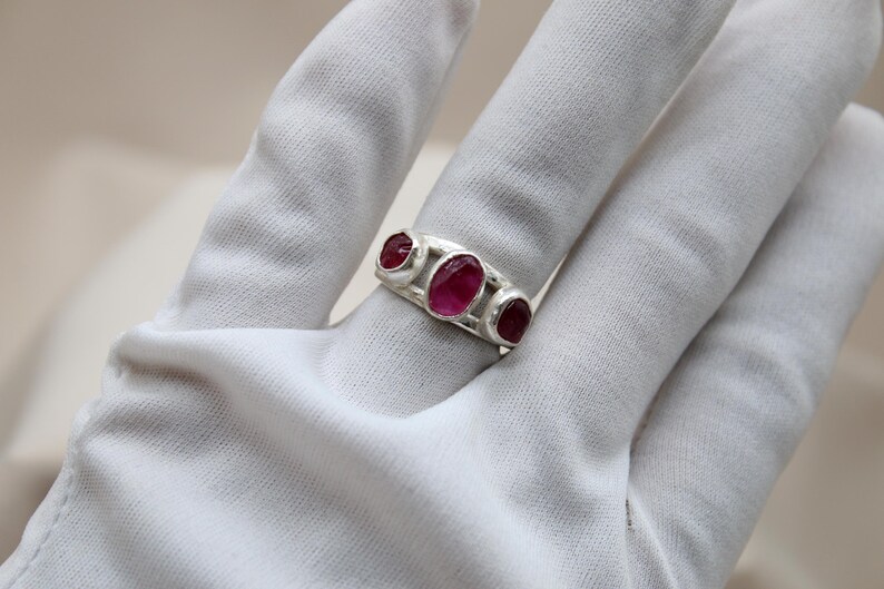 Pu&ograve; includere: Un anello d'argento con tre pietre preziose rosa di forma ovale incastonate nella fascia.
