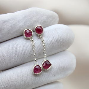 Op de afbeelding: Een paar zilveren oorbellen met roze edelstenen. De oorbellen hebben een hangend ontwerp met twee edelstenen aan elke oorbel.