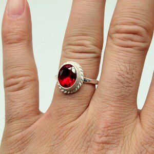 Op de afbeelding: Een zilveren ring met een rode ovale edelsteen in een decoratieve zetting.