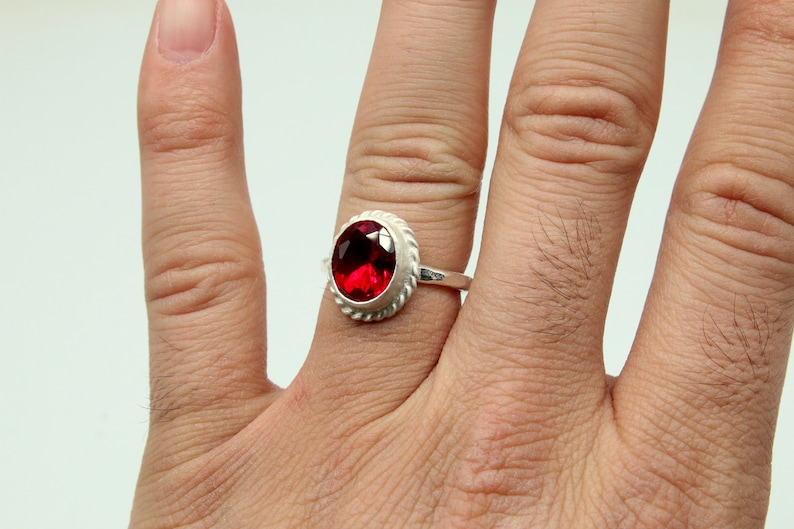 Op de afbeelding: Een zilveren ring met een rode ovale edelsteen in een decoratieve zetting.