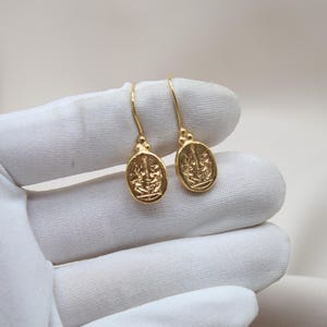 May include: A pair of gold-toned earrings with a detailed design. The earrings are oval-shaped and have a dangling design.