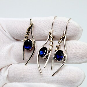 May include: A pair of silver earrings with blue gemstones and gold accents. The earrings are designed with a curved, abstract shape.