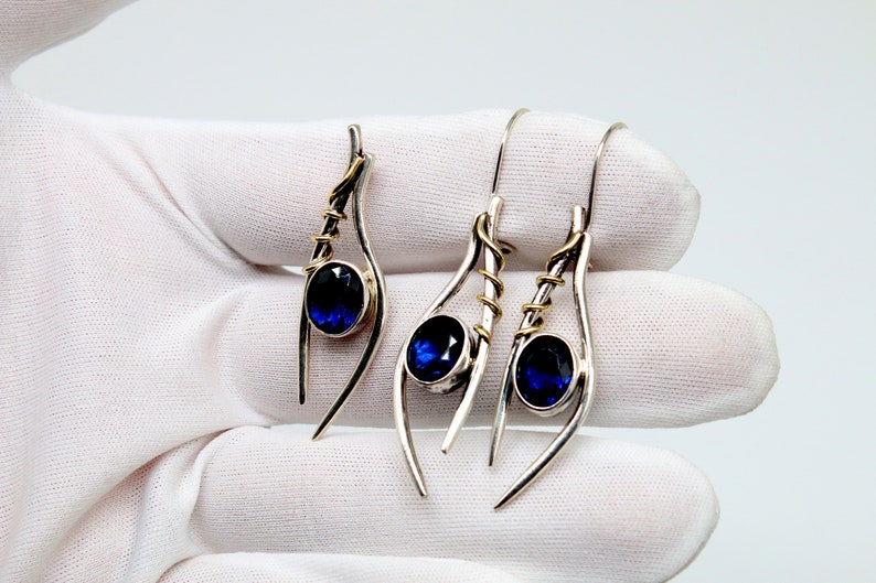 May include: A pair of silver earrings with blue gemstones and gold accents. The earrings are designed with a curved, abstract shape.