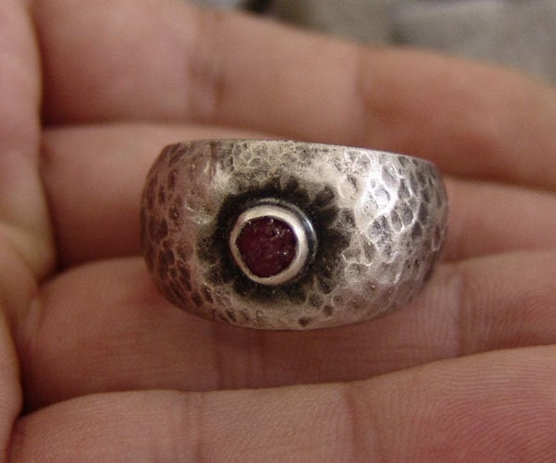 May include: A silver ring with a hammered texture and a red gemstone set in the centre.