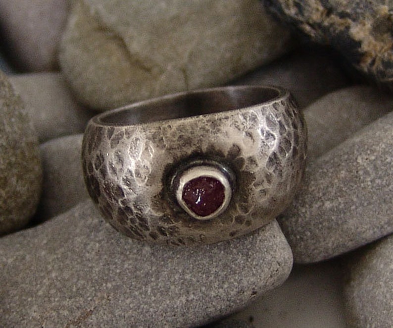 May include: A silver ring with a hammered texture and a red gemstone set in the centre.