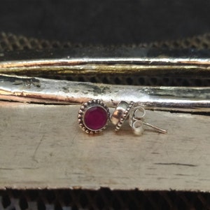 May include: A pair of silver stud earrings with a small, round, red gemstone in the center of each earring.