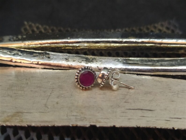 May include: A pair of silver stud earrings with a small, round, red gemstone in the center of each earring.