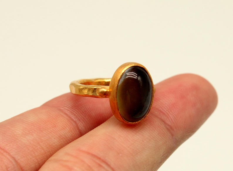 May include: A gold ring with a dark brown oval gemstone. The ring band is textured.