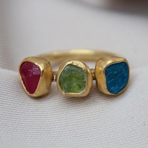 May include: A gold ring with three faceted gemstones. The stones are red, green, and blue.