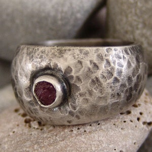 May include: A silver ring with a hammered texture and a single, round, pink gemstone set in the centre.